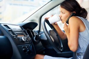 girl on a cell phone and drinking coffee while driving