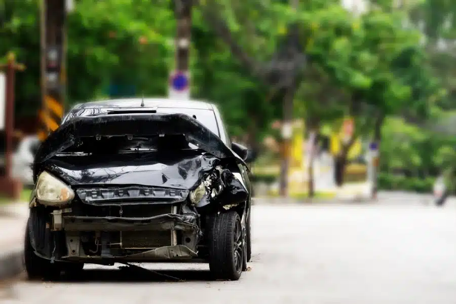 A black car with its front end smashed in, causing the car to be totaled but still possibly drivable.