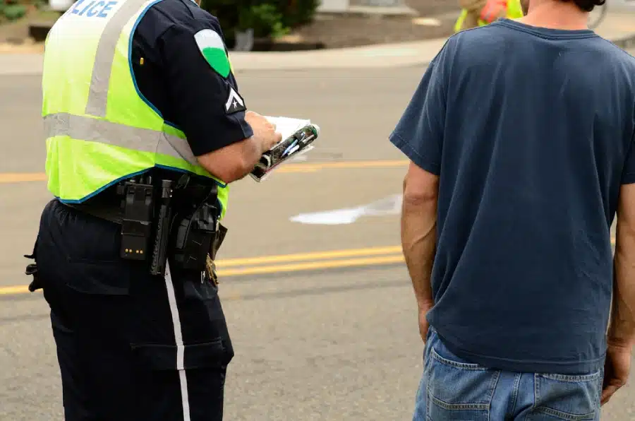 A law-enforcement officer at the scene of a single-vehicle accident, writing the crash report.