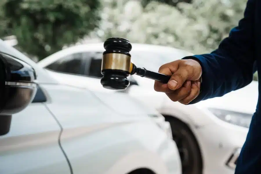 A judge holds a wooden gavel, standing in front of multiple vehicles, upholding the difference between the right to travel and the right to drive.