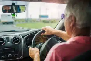 An elderly man behind the wheel of his vehicle, exercising his driving privilege.